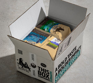 A shipping box open to see its contents inside are coffee bags with he Sloffee logo on it and the side of the box reads "A bold taste a bolder impact Sloffee.Coffee"